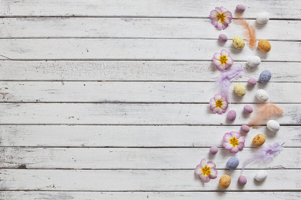 Top view of colored feathers and Easter eggs with space for your text on white wooden background. Easter concept.