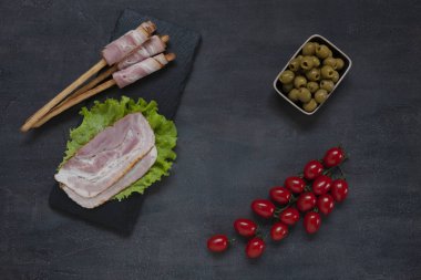 Geleneksel Pancetta pastırması turşulu zeytin, domates, yeşil salata yaprağı, şarap ve Grissini ekmeği ile servis edilir. Kapat, üst görünüm siyah arkaplan
