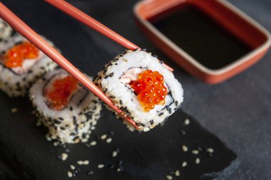 Kırmızı havyarlı, soya soslu ve çubuklu Japon yengeci mus suşisi. Üst görünüm, siyah beton arkaplanı kapat