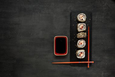 Taş tahtada soya soslu ve çubuklu Japon yengeci mus suşisi. Üst görünüm, siyah beton arkaplanı kapat