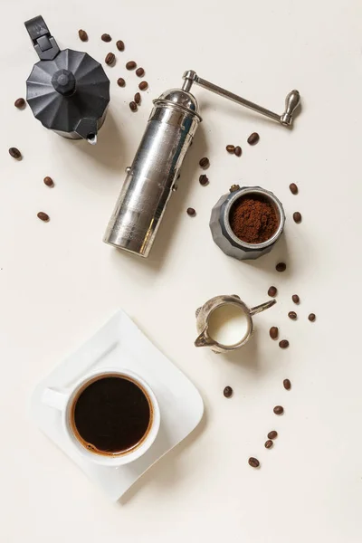 Cup of coffee, coffee mill, coffee pot and creamer with cream on the table. Top view, close up