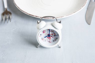 Alarm saati, çatal ve bıçaklı beyaz tabak, aralıklı oruç kavramı, ketojenik diyet, kilo kaybı.