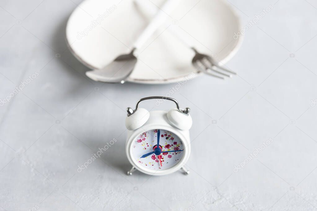 Alarm clock, White plate with spoon and fork, Intermittent fasting concept, ketogenic diet, weight loss