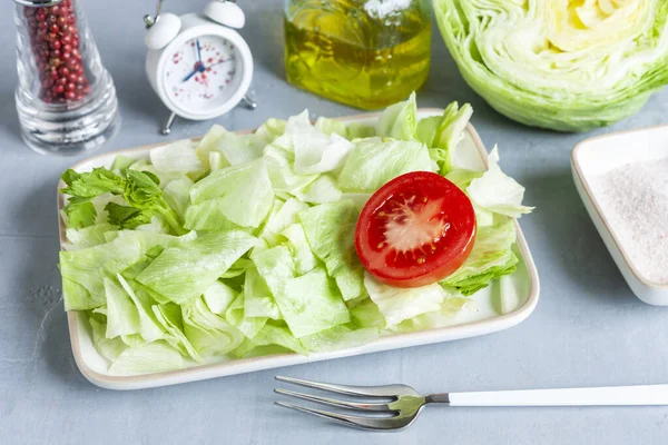 Alarm clock and plate with green iceberg lettuce, tomatoe, olive oil,  Intermittent fasting concept,  diet, weight loss