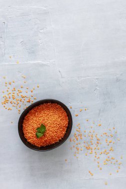 Açık gri arkaplanda siyah tabakta kırmızı mercimek.