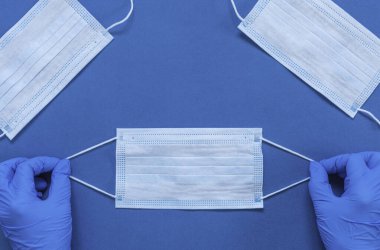 Tıbbi eldivenlerdeki eller, COVID-19 Coronavirus 'a karşı korunmak için hijyenik maske ve cerrahi maske tutuyor. 