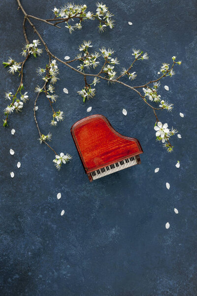Miniature copie of the piano with blossoming cherry tree branches. Top view, close-up on classic blue background	