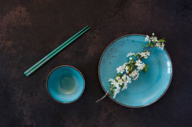 Mavi tabakta çiçek açan kiraz ağacı dalları ve koyu arkaplanda çubuklarla servis edilen bahar Japon yemekleri konsepti.