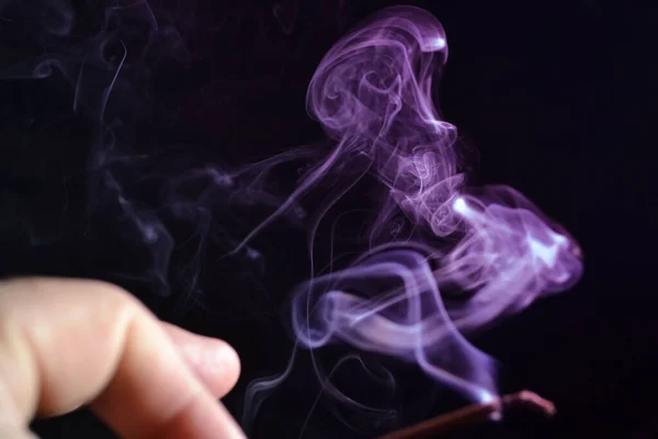 Mano sostiene un palo de incienso juego de humo sobre un fondo oscuro — Foto de Stock