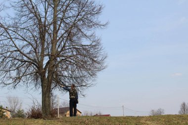 Bir adam yalnız bir ağaca yaslanarak tepesinde duruyor. İlkbaharın başlarında. Adam elini ağaca yaslanmış yüksek bir hillock üzerinde duruyor. Adam düşünüyor ve başka bir yere bakıyor. Sırtına değdi