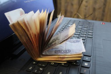 Kağıt para dizüstü bilgisayarın klavyesinde / banknot destesinin fotoğrafında yatıyor. Rusya 'nın parası siyah bir dizüstü bilgisayarın klavyesinde yatıyor..