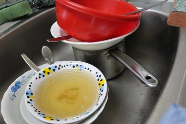 dirty dishes in a metal sink in the kitchen / photo of dirty dishes in the kitchen. stainless steel sink. it contains a pot and plates.