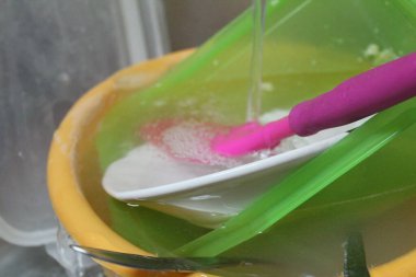 Kirli bulaşıklar mutfak lavabosunda ve kirli plastik tabakların fotoğrafında. Metal bir lavaboda. Musluktan su akıyor..