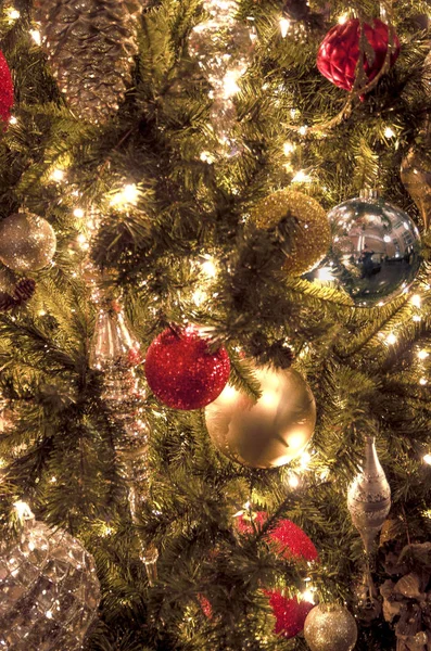 Close up of Christmas ornaments shining in the twinkle lights while hanging a brightly lit Holiday tree
