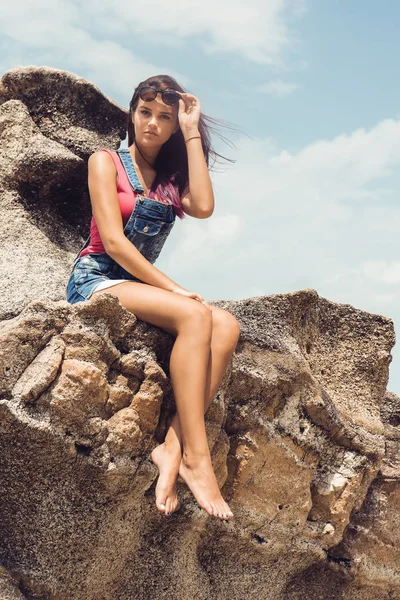 Dziewczyna w denim ogólnej na skały plaża. — Zdjęcie stockowe