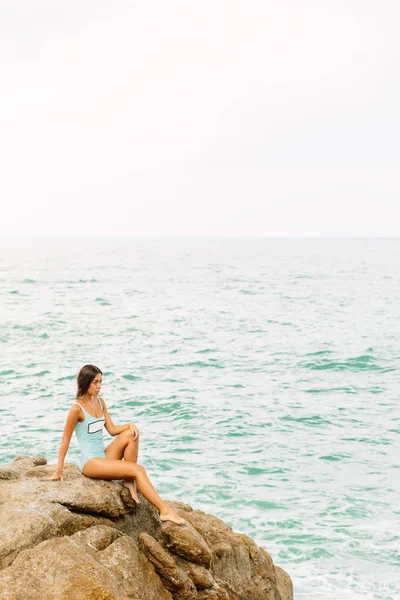 Beautiful girl in blue swimsuit sit on big stone. — Stock Photo, Image