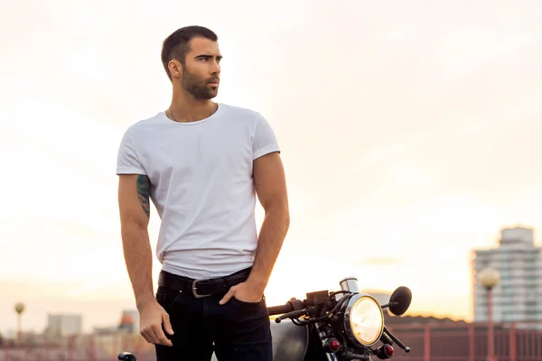 Brutal man near his cafe racer custom motorbike.