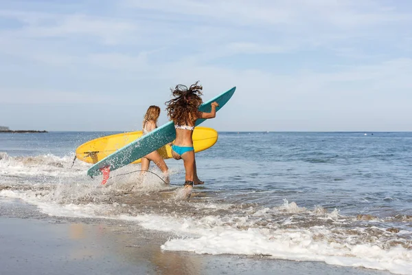 Zwei schöne Surfermädchen am Strand gehen ins Wasser. — Stockfoto