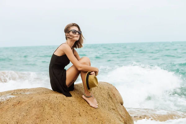 Schattig meisje in zwarte zomer jurk op grote stenen. — Stockfoto