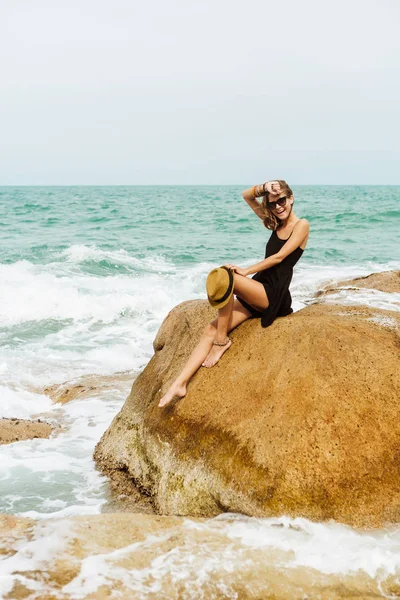 Menina bonito em vestido de verão preto em pedras grandes . — Fotografia de Stock