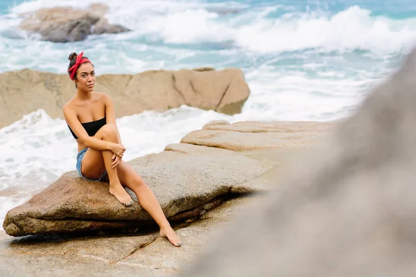 Menina bonita em shorts curtos sentar-se em grandes pedras . — Fotografia de Stock