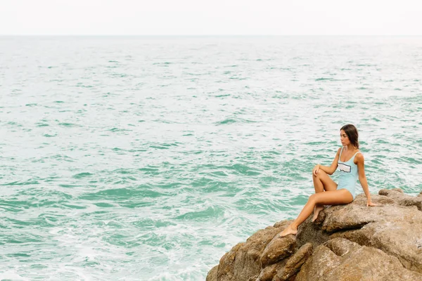 Beautiful girl in blue swimsuit sit on big stone. — Stock Photo, Image