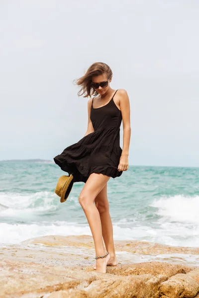 Menina bonito em vestido de verão preto em pedras grandes . — Fotografia de Stock