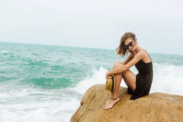 Menina bonito em vestido de verão preto em pedras grandes . — Fotografia de Stock