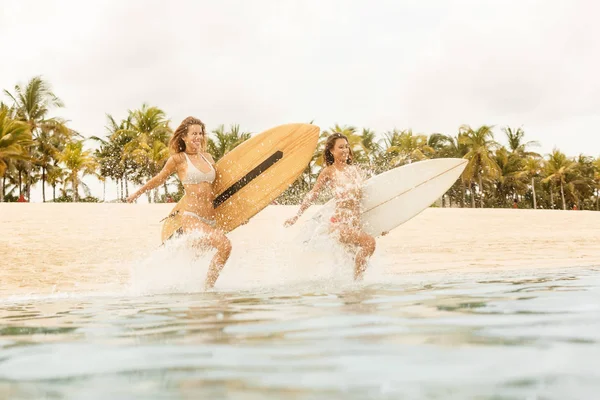 Two beautiful surfer girls at the beach go into the water. — Stock Photo, Image