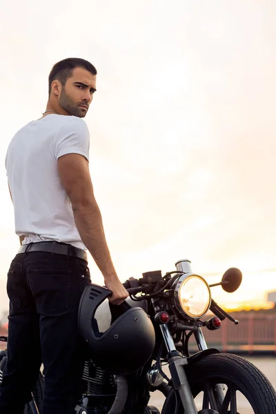 Brutal man near his cafe racer custom motorbike.