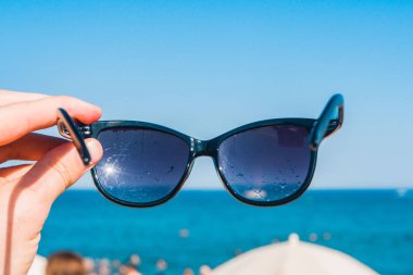 Sahilde, parlak yaz günü bir elinde güneş gözlüğü