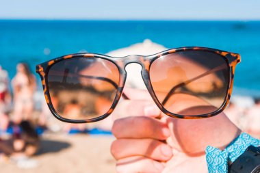 Sahilde, parlak yaz günü bir elinde güneş gözlüğü