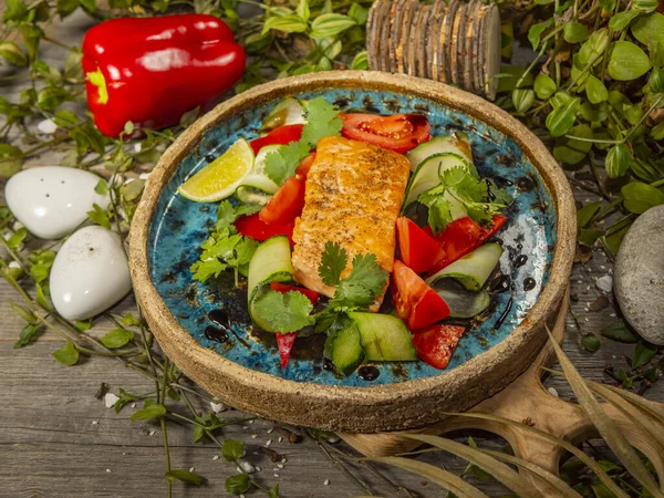 Steak de saumon frais savoureux aux concombres, tomates et autres légumes avec sauce, sur une assiette artisanale — Photo