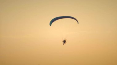 Gün batımında bir adam şehirde motorlu bir paraglider uçuruyor. iyi akşamlar