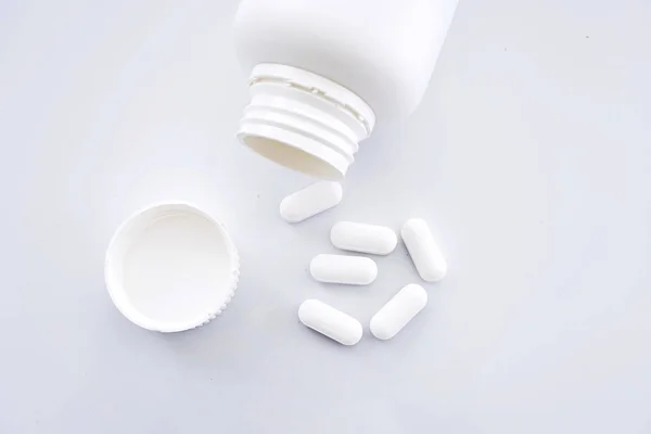 Cápsulas blancas que se derraman de un frasco de medicamentos recetados —  Fotos de Stock