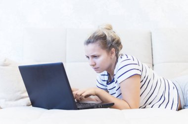 Sarışın kız evinde dizüstü bilgisayarla kanepede oturuyor ve internetten iletişim kuruyor. Sosyal ağlar. tarihler.
