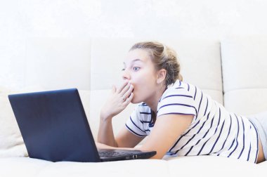 Sarışın kız evinde dizüstü bilgisayarla kanepede oturuyor ve internetten iletişim kuruyor. Sosyal ağlar. tarihler.