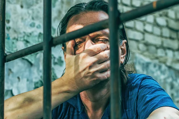 Un hombre deprimido sostiene sus manos en las rejas de la prisión. Prisionero por el crimen. Malas condiciones. Grito, desesperación, dolor, hambre . — Foto de Stock