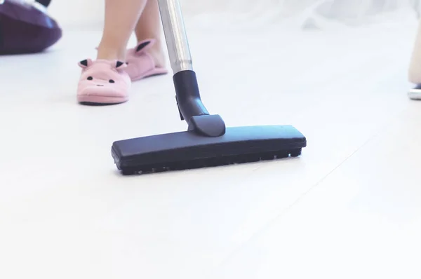 Uma rapariga de chinelos e um roupão de banho a aspirar o chão num apartamento. foco seletivo. grão de filme . — Fotografia de Stock