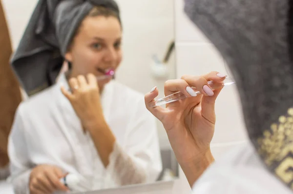 En flicka med en handduk på huvudet borstar tänderna på morgonen framför en spegel i badrummet. selektivt fokus. Filmkärnor. — Stockfoto