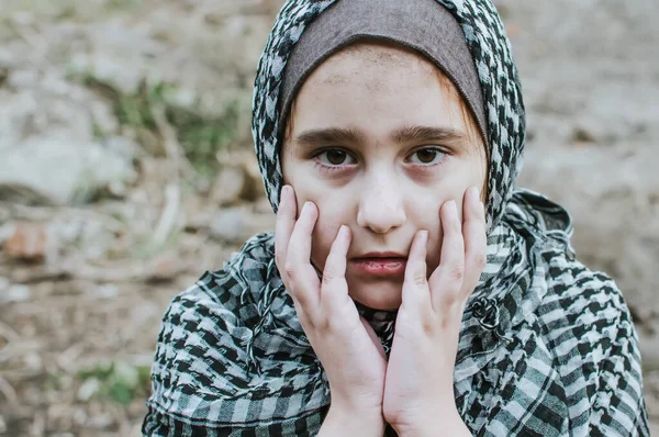 A refugee child in the war, a Muslim girl with a dirty face on the ruins, the concept of peace and war, the child is crying and waiting for help. — Stock Photo, Image