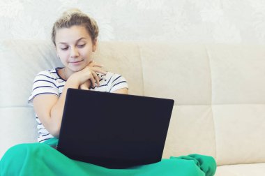 Sarışın kız evinde dizüstü bilgisayarla kanepede oturuyor ve internetten iletişim kuruyor. Sosyal ağlar. tarihler.