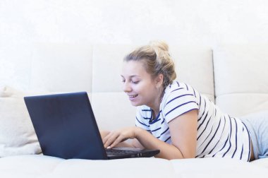 Sarışın kız evinde dizüstü bilgisayarla kanepede oturuyor ve internetten iletişim kuruyor. Sosyal ağlar. tarihler.