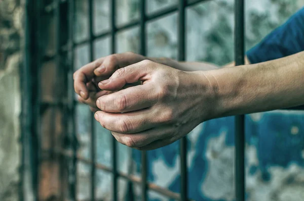 Um homem deprimido segura as mãos nas grades da prisão. Prisioneiro pelo crime. Pobres condições. Grito, desespero, dor, fome . — Fotografia de Stock