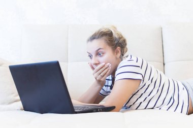 Sarışın kız evinde dizüstü bilgisayarla kanepede oturuyor ve internetten iletişim kuruyor. Sosyal ağlar. tarihler.