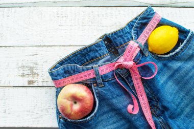 Elma ve limonlu kot pantolon, ahşap arka planda. Üzerinde kemer yerine mezura olan kot pantolon. Bel çevresindeki ölçü bandıyla kot pantolon. Sağlıklı yaşam tarzı kavramı