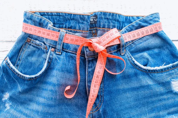 Pantalon haut en denim, sur fond bois. Jeans bleu avec un ruban à mesurer au lieu d'une ceinture. jeans avec un ruban à mesurer autour de la taille. Le concept d'un mode de vie sain et d'une alimentation saine . — Photo