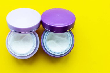 Sarı arka planda yüz kremi olan gri kavanozlar. Cilt bakımı.