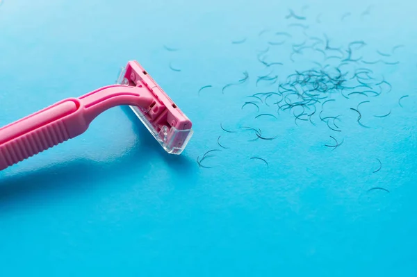 Ženské holicí strojek růžové a vlasy na modrém pozadí. Koncept ženského holení. — Stock fotografie