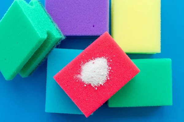 Cleaning powder on a red dishwashing sponge next to multi-colored sponges on a blue background. The concept of homework.